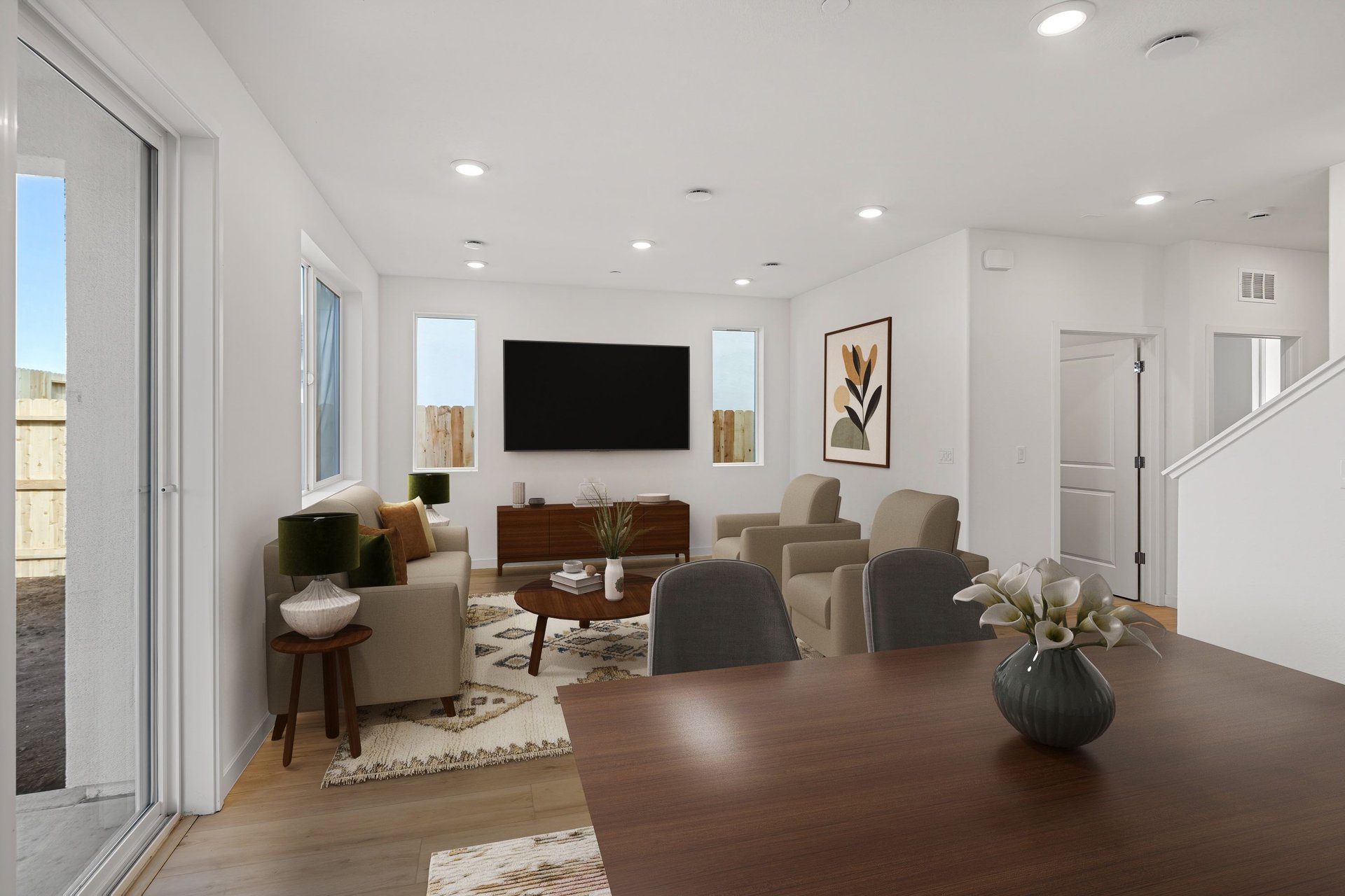 great room with dark wood tables, television on wall, multiple windows, tan sofa & two chairs, and wood floors