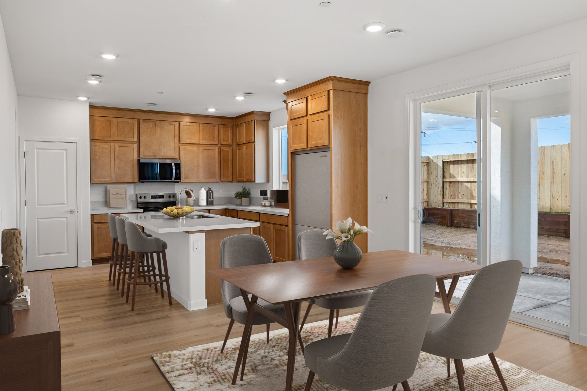 dining room with wood table, four gray chairs, wood floors, and sliding glass door to the back covered patio