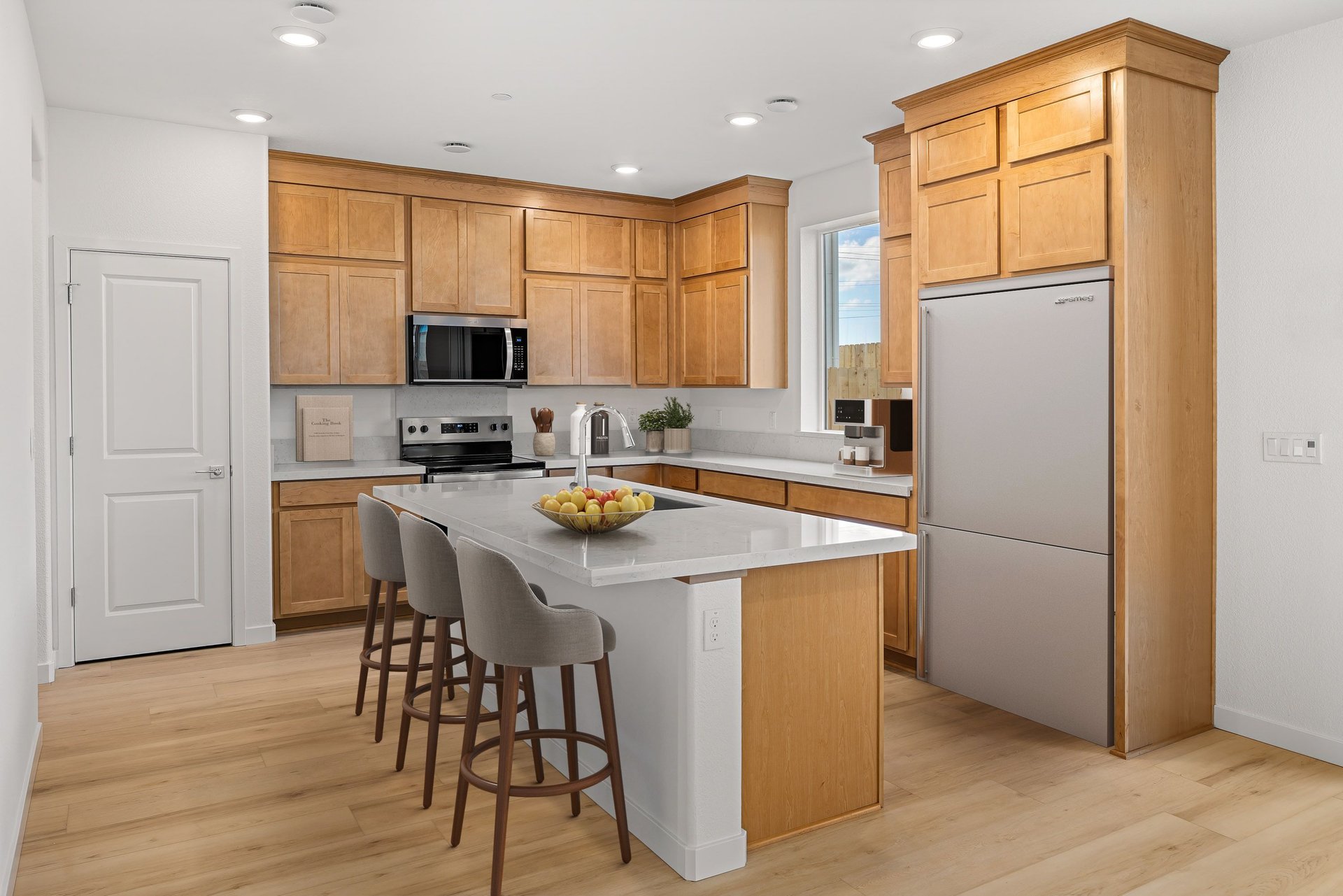 kitchen with wood floors, rye-colored cabinets, white counters, island, and window