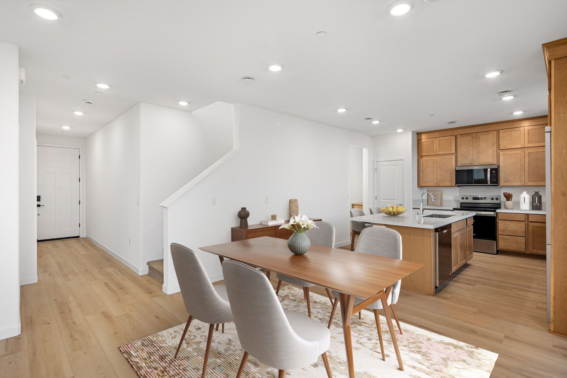 dining room with wood table, four gray chairs, white walls, wood floors, and view of entry foyer