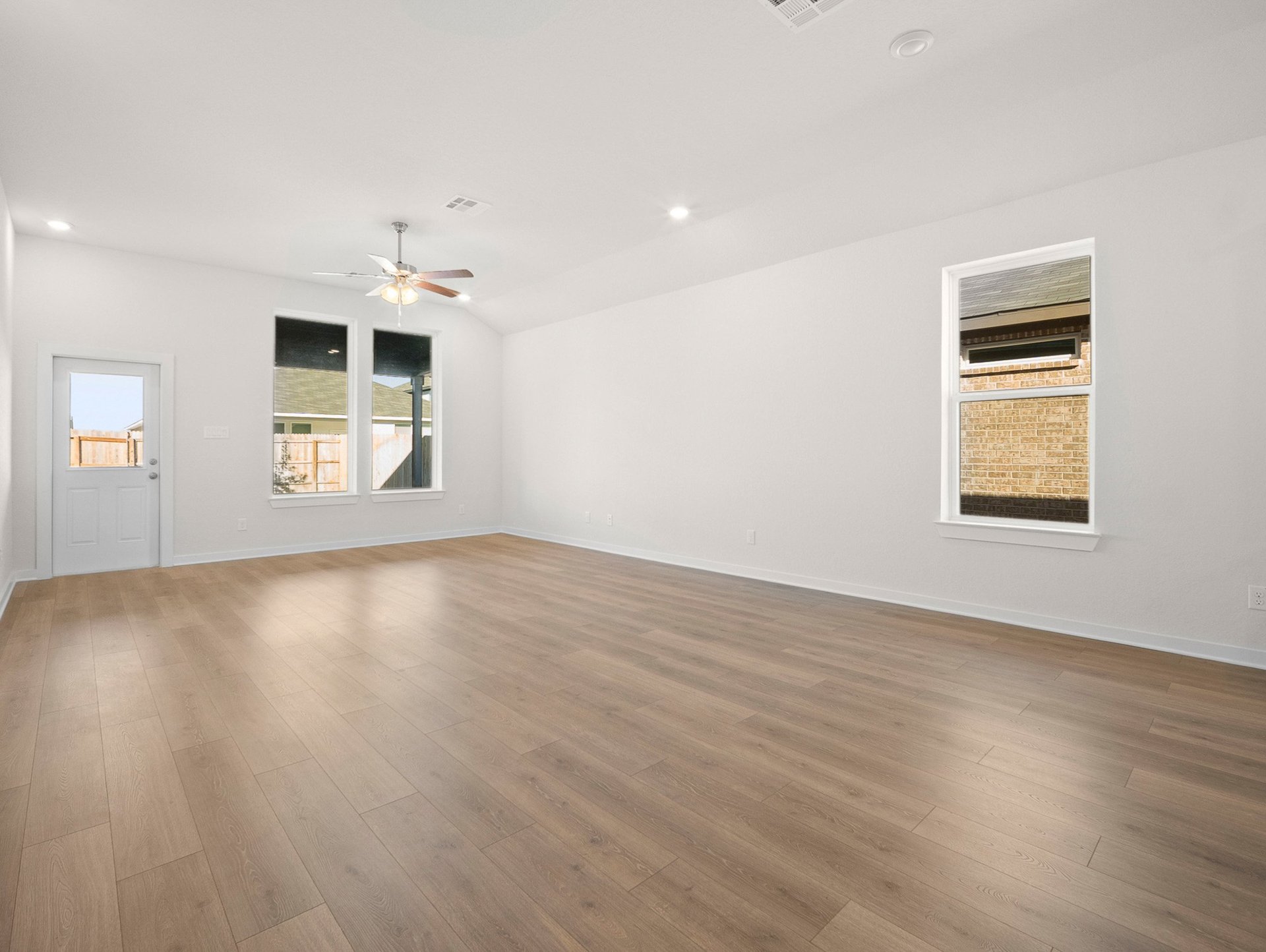great room with brown flooring, windows & a ceiling fan