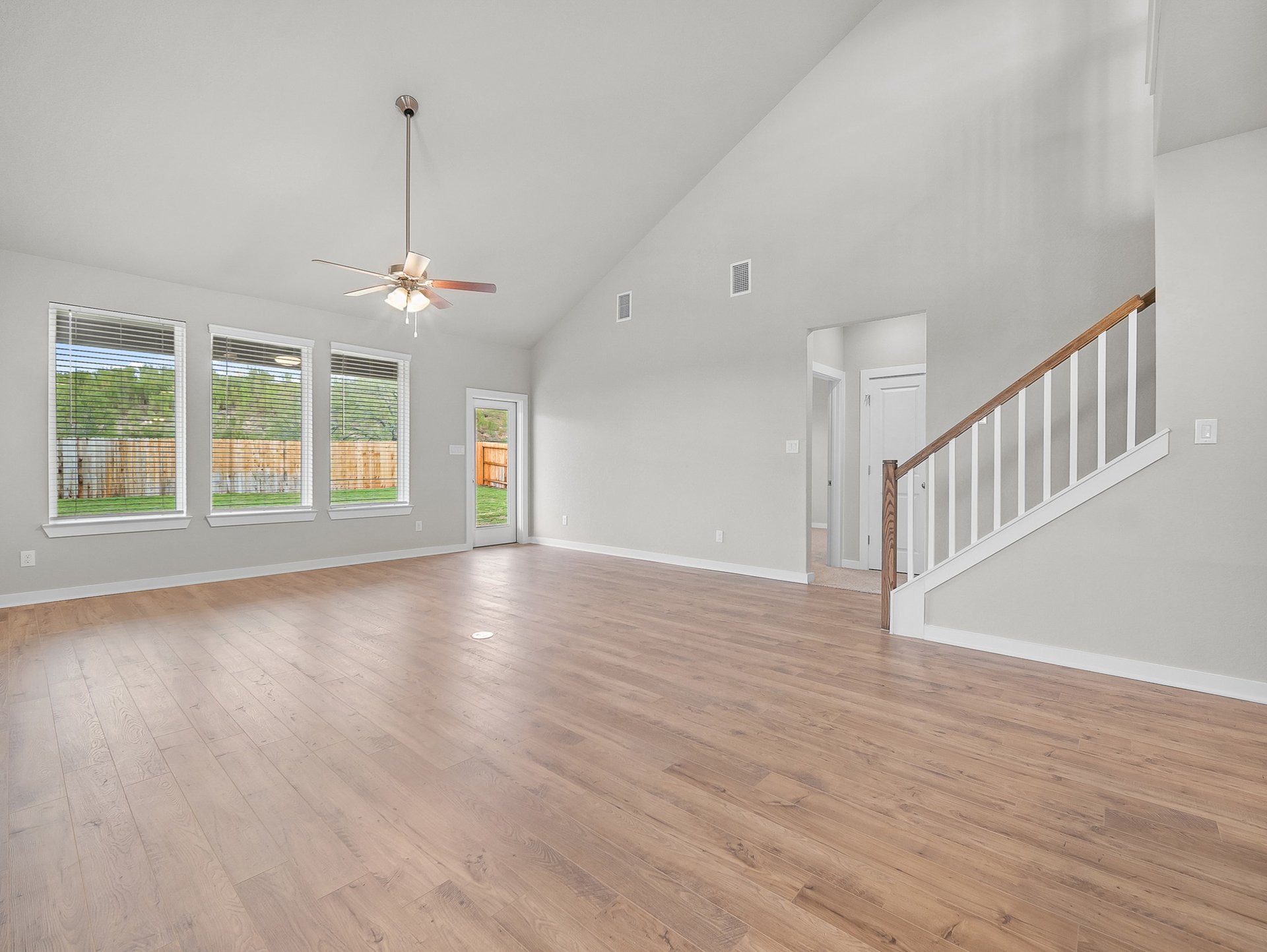 great room with brown flooring, windows & a ceiling fan