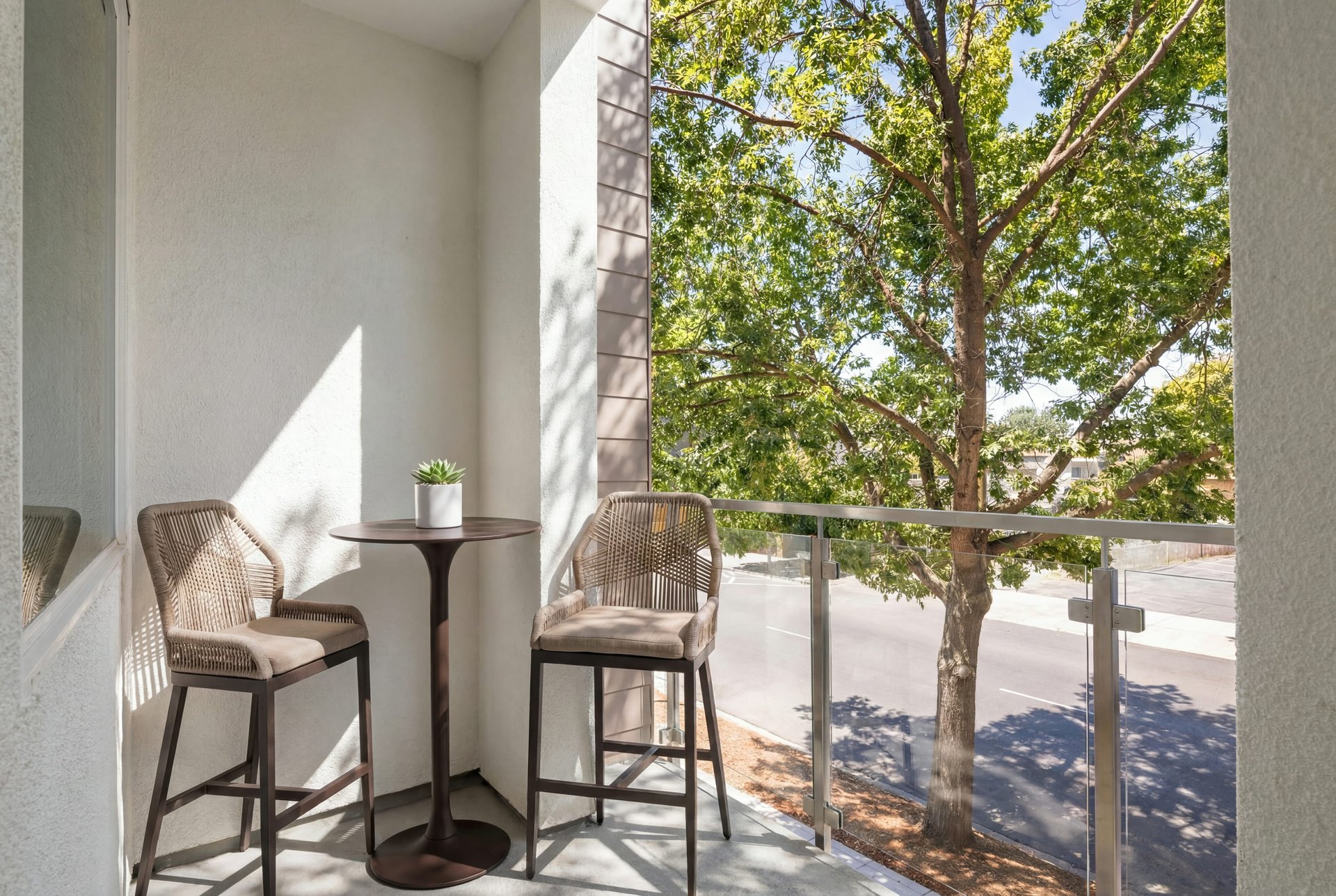 balcony with glass enclosure, view to street, small brown pub table, and two chairs