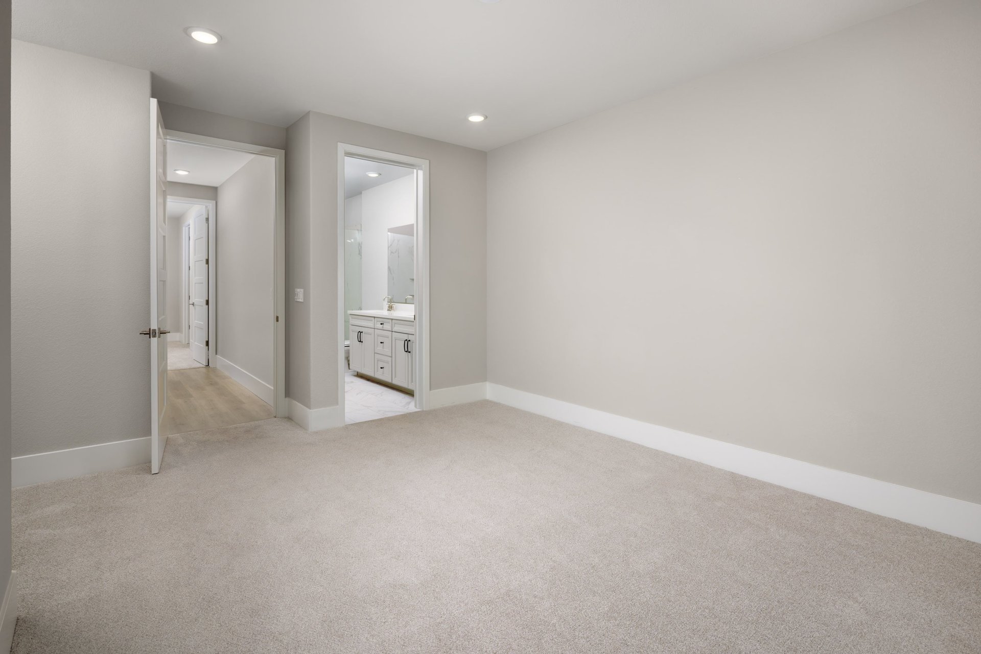 bedroom with light tan carpet & walls, recessed ceiling lights, and attached bathroom