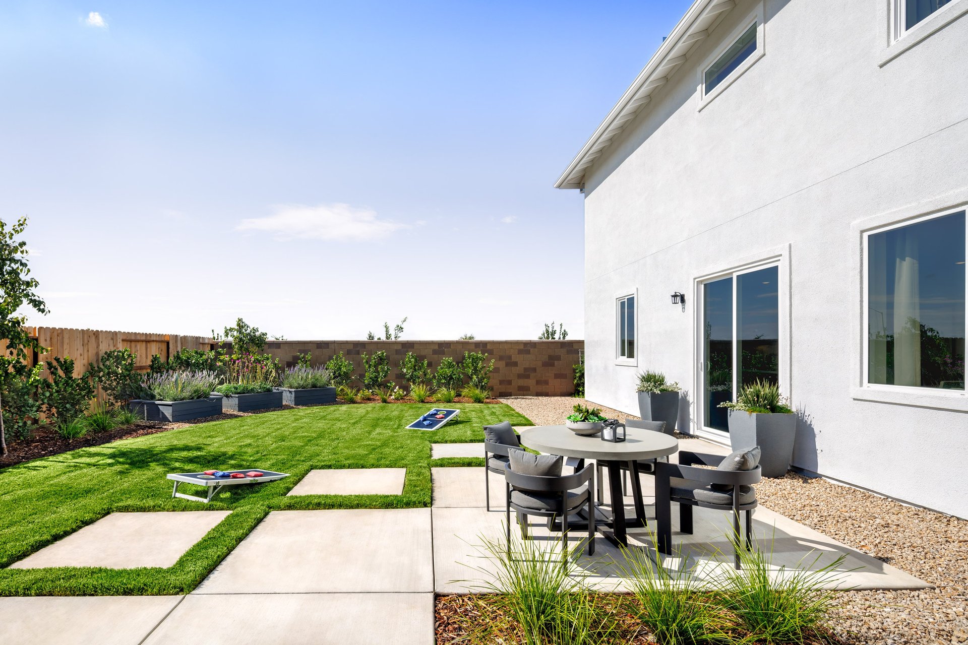 backyard with grass, concrete with round table & four gray chairs, and raised garden beds