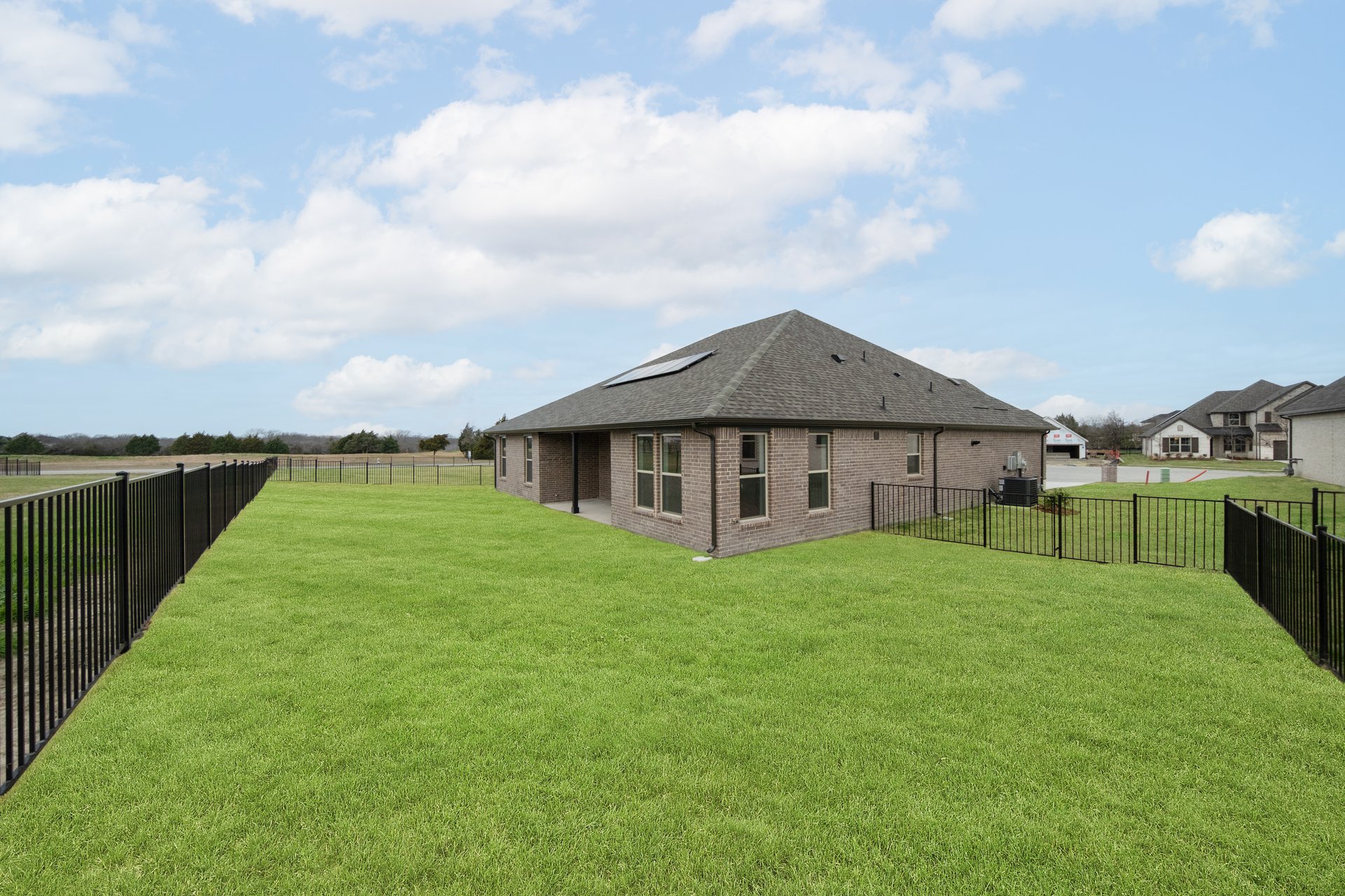 large backyard with wrought iron fence, grass, and covered patio