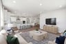 great room with wood floors, blue & tan patterned area rug, television on wall with light wood cabinet below, and two tan sofas