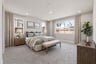 bedroom with tan carpet, multiple windows, tan upholstered bed with sage green bedding, and wood dresser & nightstands