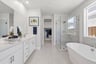 bathroom with white cabinets & counters, two sinks, tan tile floors, walk-in shower, and window above freestanding tub