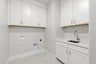 laundry room with white upper & lower cabinets, sink, and tan tile floors