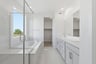 bathroom with white cabinets and counters, two sinks, walk-in shower, and large window above tub