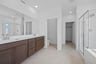 bathroom with brown cabinets, white counters, two sinks, and tan tile floors with walk-in shower