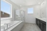 bathroom with tan tile floors, espresso cabinets, white counters, two sinks, walk-in shower, and window above soaking tub