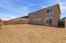 back exterior of tan two-story home with unfinished backyard and wood fence