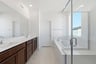 bathroom with brown wood cabinets, white counters, two sinks, walk-in shower, and large window above soaking tub