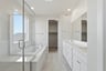 bathroom with white cabinets, white counters, two sinks, walk-in shower, and window above tub