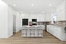 kitchen with white cabinets & counters, tan tile backsplash, wood floors, bowl of fruit on island, and three gray & gold barstools