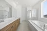 bathroom with light wood cabinets, white counters, two sinks, walk-in shower, and window above soaking tub