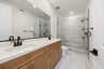bathroom with gray and white patterned tile floors, wood cabinets, white counters, two sinks, and large walk-in shower