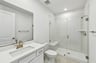 bathroom with white cabinets & counters, gold hardware & fixtures, and large walk-in shower with bench
