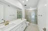 bathroom with white cabinets & counters, two sinks, gold faucets, and large walk-in shower with frameless glass enclosure