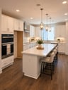 kitchen with white cabinets & counters, wood floors, and four white barstools at island