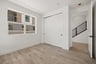 bedroom with window, light wood floors, closet, and view of black entry stair rail