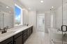 bathroom with black cabinets, white counters, two sinks, white & gray tile floor and wall, freestanding tub, and walk-in shower