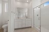 bathroom with white cabinets & counters, two sinks, tan tile floor, and large walk-in shower with glass enclosure