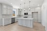kitchen with light gray cabinets, light wood floors, white counters, three brushed nickel pendants above island, and window