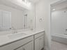 secondary bathroom with dual sinks, soaking tub and white cabinets