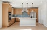 kitchen with light wood cabinets, blue tile backsplash, white counters, and three gold pendant lights above island