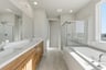 bathroom with light wood cabinets, white counters, two sinks, walk-in shower, and window above tub