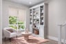 open library space with white built-in bookshelves, light pink area rug, white accent chair, and window