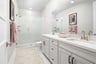 bathroom with white cabinets & counters, two sinks, large neutral area rug, towel bar with pink towels, and large walk-in shower