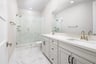bathroom with white cabinets & counters, two sinks, and large walk-in shower with glass enclosure