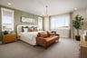 bedroom with green accent wall behind white bed, gray carpet, three windows, and brown leather sofa at foot of bed
